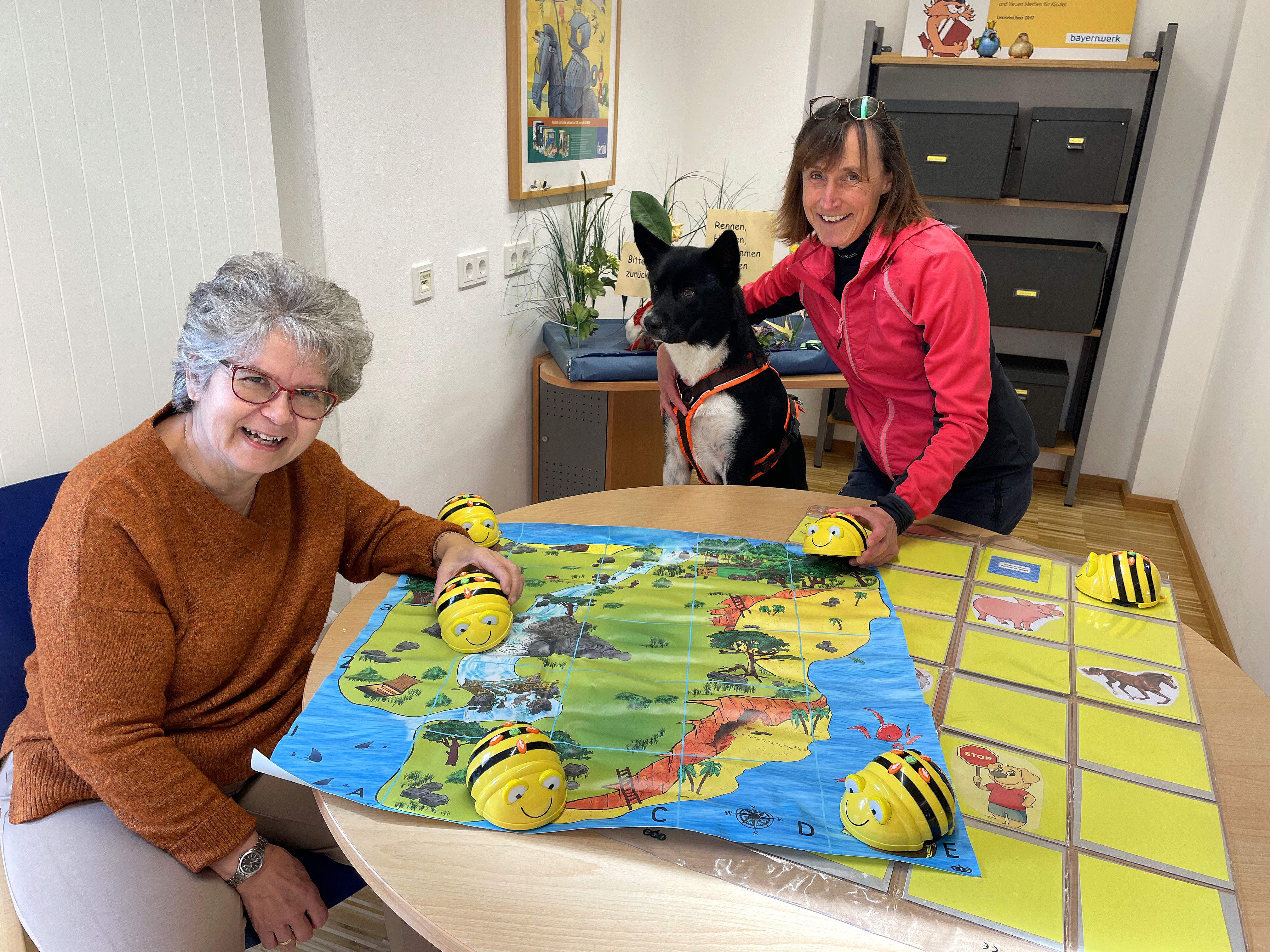Freuen sich auf die neuen Bee-Bot®-Spielstunden: Barbara Lohmaier (links), Bibliothekshund Benny und Bibliotheksleiterin Karola Künzl (rechts).
