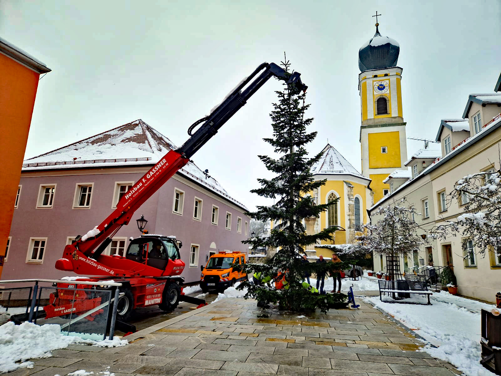 Kranarm stellt Tannenbaum auf, Gebäude und Kirche im Hintergrund